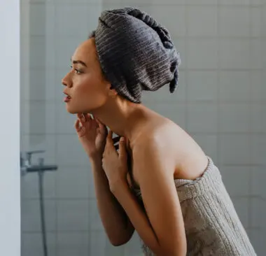 A woman in a towel turban looking at the mirror