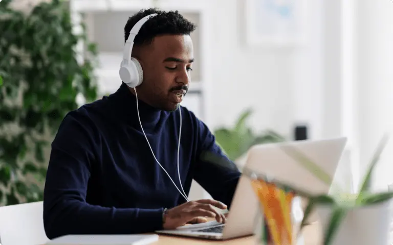 Person wearing headphones, using a laptop at a desk, possibly engaged in an online training session.