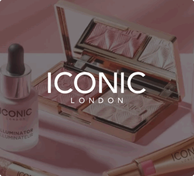 Prodotti per il trucco ICONIC London, tra cui una palette di illuminanti in polvere e un illuminante in gocce, presentati su una superficie rosa.