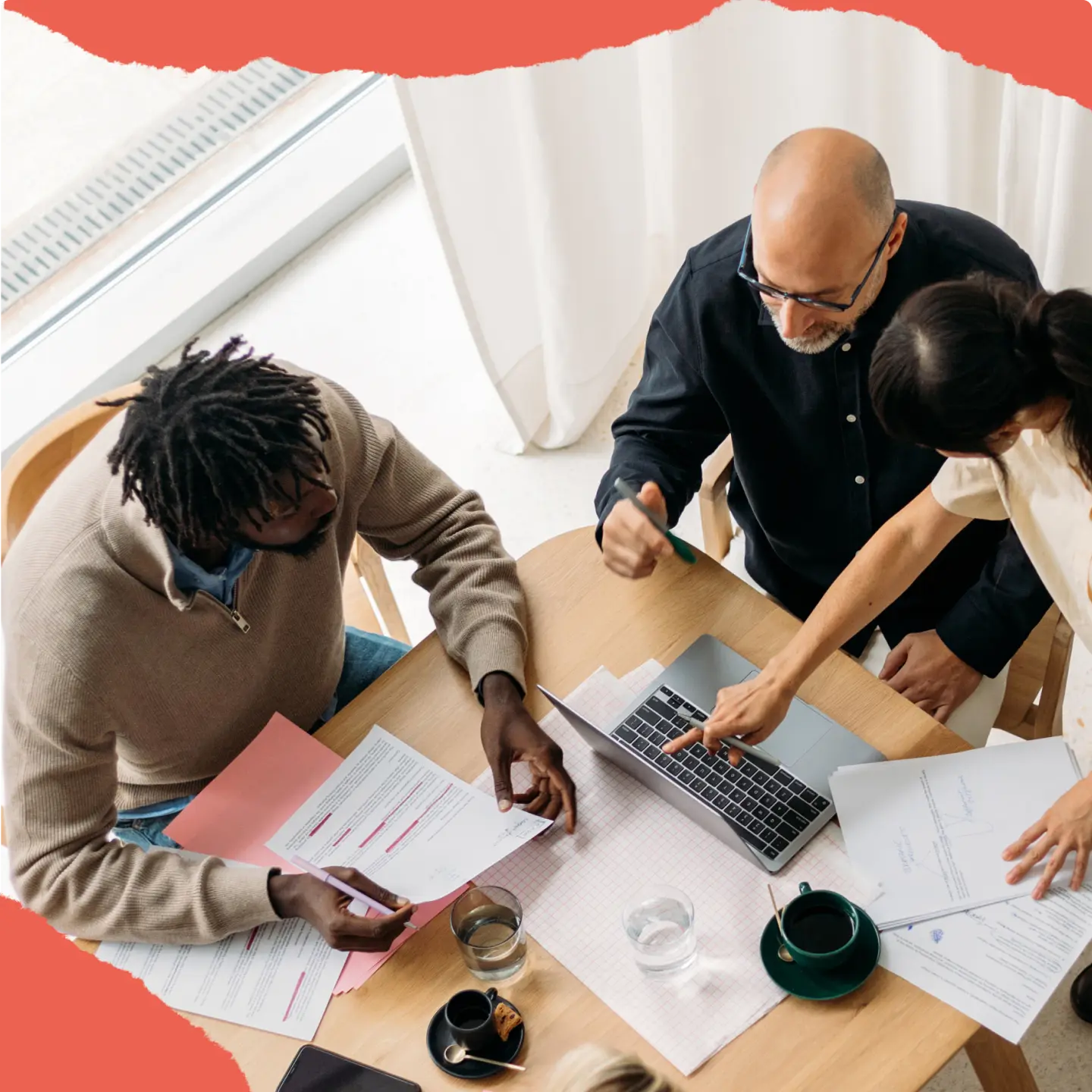 Three people collaborating at a table with documents and a laptop.