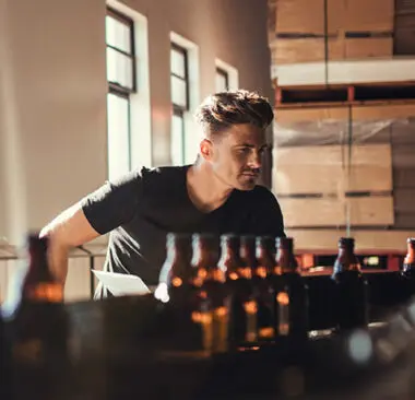 man at a bar looking over glass bottles with the sun behind him