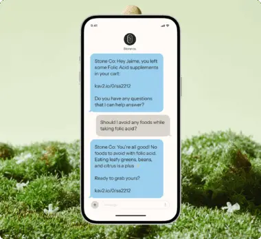 Smartphone displaying a text conversation about folic acid supplements between a customer and Stone Co. on a grassy background.