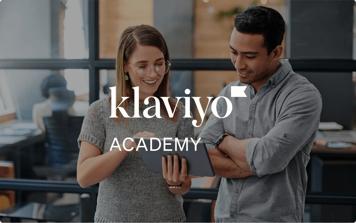 Two coworkers collaborating on an iPad in an office with Klaviyo Academy text overlay